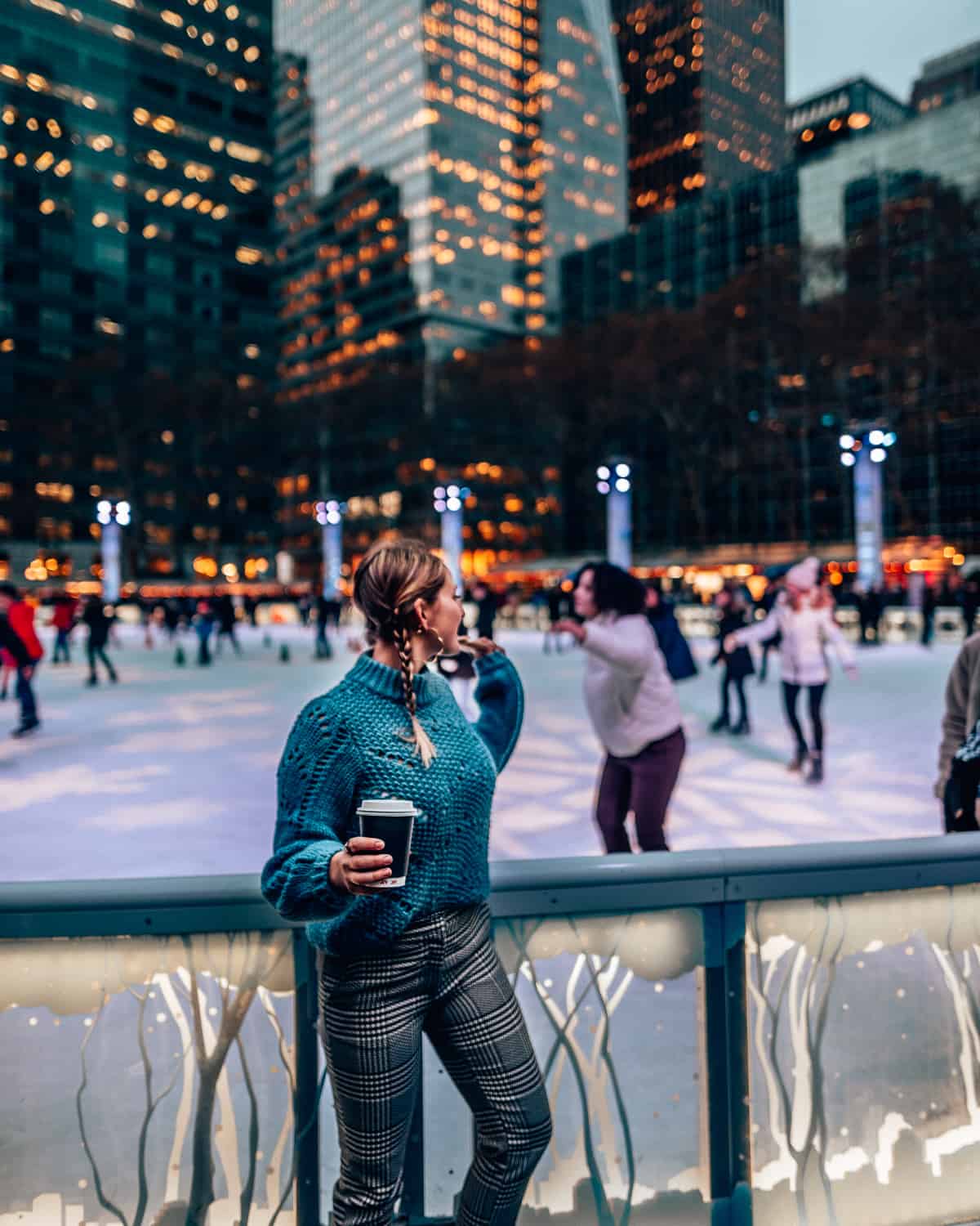 girl standing with hot chocolate standing in front of an ice skating rink