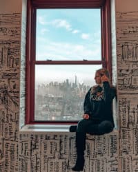 chica sentada en una ventana con vistas a una ciudad